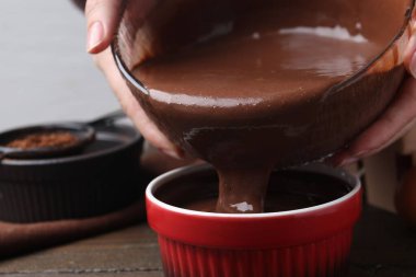 Kadın, ahşap masadaki yemek kabına çikolata hamuru döküyor, yakın plan.