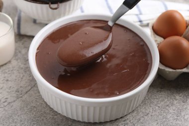 Gri masadaki kaşıkla kaseden sıvı çikolata hamuru alıyoruz. Yakın plan.