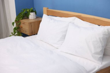 Sıcak, temiz çarşaflı yatak ve mavi duvarın yanında komodin.