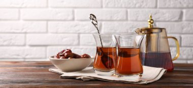 Cam bardaklardaki lezzetli Türk çayı, ahşap masadaki hurma ve çaydanlık beyaz tuğla duvara karşı, yakın plan. Metin için boşluk