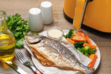 Lezzetli ızgara balık, sebze, sos ve tava ahşap masada, yakın plan.