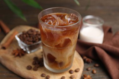 Tasty iced coffee in glass, milk and beans on wooden table, closeup