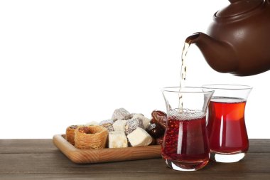 Geleneksel Türk çayını cam bardaklara ve tatlıları beyaz arka planda, yakın planda, ahşap masaya dökerek