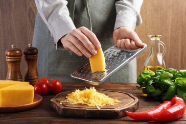 Ahşap masada peynir rendeleyen kadın, yakın plan.