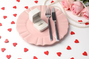 Romantik yemek için güzel bir masa, nişan yüzüğü ve beyaz arka planda güllerle dolu bir kutu.