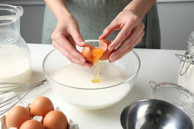 Hamur yapmak (sıvı hamur). Beyaz masadaki kaseye yumurta ekleyen kadın, yakın plan.