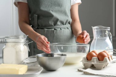 Hamur yapmak (sıvı hamur). Beyaz masadaki kaseye yumurta ekleyen kadın, yakın plan.