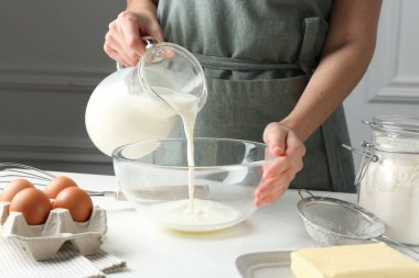 Hamur yapmak (sıvı hamur). Beyaz masadaki kaseye süt döken kadın, yakın plan.