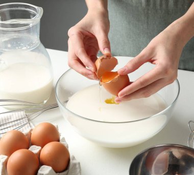 Hamur yapmak (sıvı hamur). Beyaz masadaki kaseye yumurta ekleyen kadın, yakın plan.