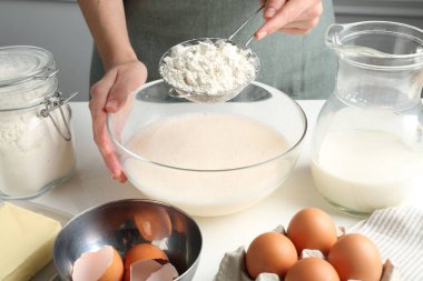 Hamur yapmak (sıvı hamur). Beyaz masada un yiyen bir kadın. Kapalı alanda, yakın plan.