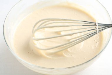 Beyaz masa üzerinde hamurlu kase ve çırpma (sıvı hamur), yakın plan