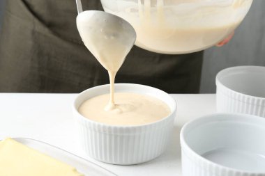 Kadın hamur hamurunu (sıvı hamur) içerideki masada yemek tabaklarına döküyor, yakın plan.