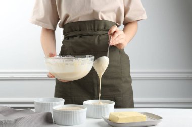 Kadın hamur hamurunu (sıvı hamur) içerideki masada yemek tabaklarına döküyor, yakın plan.