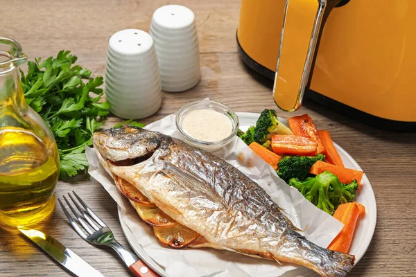 Lezzetli ızgara balık, sebze, sos ve tava ahşap masada, yakın plan.