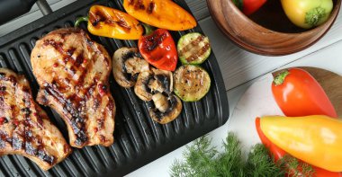 Lezzetli sebzelerle elektrikli ızgara ve beyaz ahşap masada biftekler.