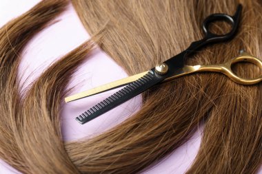 Açık mor arkaplanda güzel kahverengi saç ve makas, yakın plan.