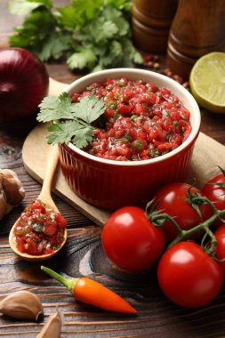 Delicious salsa sauce in bowl and ingredients on wooden table, closeup