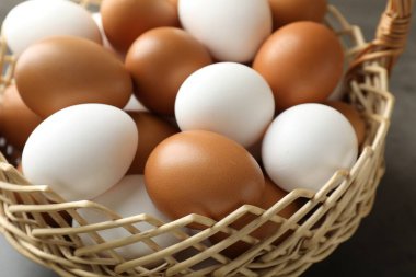 Hasır sepetin içinde çiğ tavuk yumurtası. Gri masada, yakın plan.