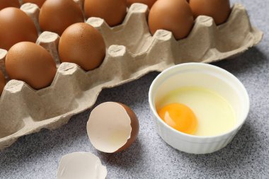 Bir sürü çiğ tavuk yumurtası ve bir tanesi gri masada kırılmış, yakın plan.