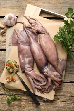 Raw squids, stuffing and parsley on wooden table, flat lay