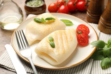 Lezzetli ızgara kalamar, domates, fesleğen ve çatal bıçak parçaları ahşap masada, yakın plan.