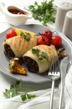 Mantar, maydanoz ve sebzelerle doldurulmuş lezzetli ızgara kalamar parçaları beyaz ahşap masada, yakın plan.