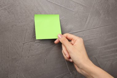 Kadın gri duvara boş yapışkan bir not yapıştırıyor, yakın plan. Metin için boşluk