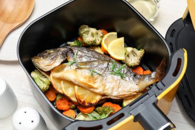 Pişmiş balık, limon ve sebzeler, tava sepetinde beyaz ahşap masada, yakın plan.