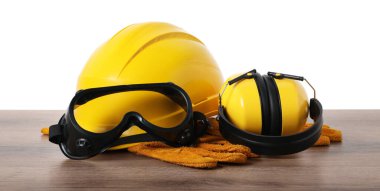 Güvenlik ekipmanları. Kasket, kulaklık, koruyucu eldivenler ve beyaz arka plana karşı ahşap masa üzerindeki gözlükler.