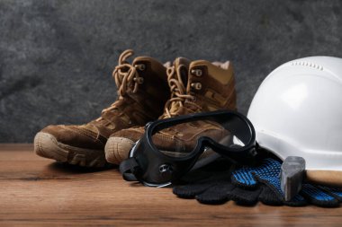 Sert şapka, koruyucu eldivenler, gözlükler, çizmeler ve çekiç tahta masada. Güvenlik ekipmanları