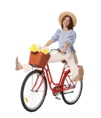 Şapkalı gülümseyen kadın beyaz arka planda bir sepet çiçekle bisiklet sürüyor.
