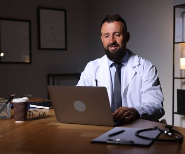 Doktor, gece vardiyası sırasında klinikteki masada dizüstü bilgisayarla çalışıyor.