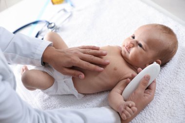 Pediyatrist bebeğin sıcaklığını hastanede termometreyle ölçüyor.