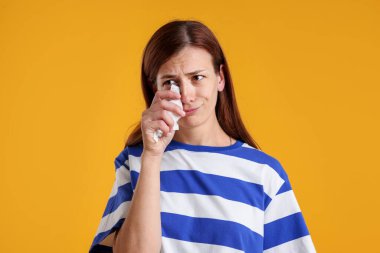 Kadın ağlıyor ve sarı arka planda gözyaşlarını siliyor.