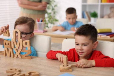 İlkokulda tahta masalarda öğretmenden ders alan küçük çocuklar, yakın çekim.