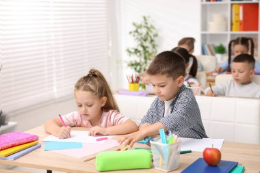 İlkokulda sanat dersi sırasında tahta masalarda oturan sevimli çocuklar.