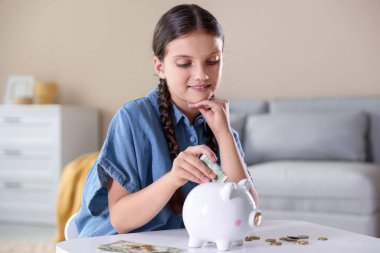 Gülümseyen küçük kız beyaz masadaki kumbaralara para yatırıyor. Cep harçlığı ve sorumluluk