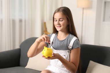 Kız cep harçlığını evdeki kanepedeki kumbaraya yatırıyor.