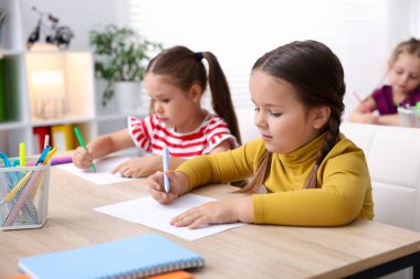 İlkokulda sanat dersi sırasında tahta masalarda oturan küçük kızlar.