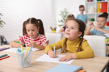 İlkokulda sanat dersi sırasında tahta masalarda oturan çocuklar.