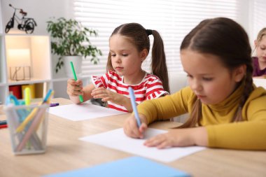 İlkokulda sanat dersi sırasında tahta masalarda oturan küçük kızlar.