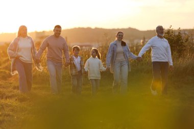 Mutlu aile gün batımında el ele tutuşup tarlada yürüyor.