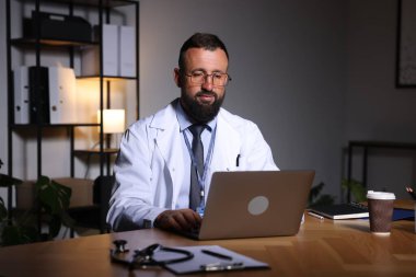 Doktor, gece vardiyası sırasında klinikteki masada dizüstü bilgisayarla çalışıyor.