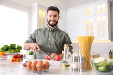 Yemek pişirme süreci. Gülümseyen adam mutfakta domates kesiyor.