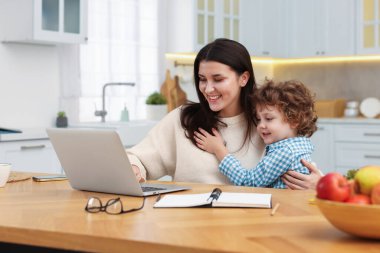 Bilgisayarla çalışan gülümseyen kadın ve oğlu ofis odasındaki tahta masada.