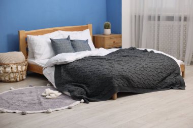 Yatak odasındaki mavi duvarın yanında çarşaflı, komodinli, sepetli büyük bir yatak. İç tasarım