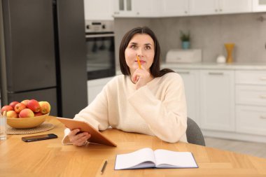 Ofisteki ahşap masada tabletle çalışan düşünceli bir kadın.