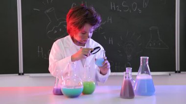 Okula dönelim. Çocuk masa başında formüllü karatahtaya karşı kimyasal araştırma yapıyor.