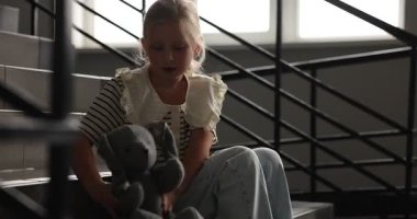 Oyuncak tavşancığı olan üzgün küçük kız içeride merdivenlerde ağlıyor.