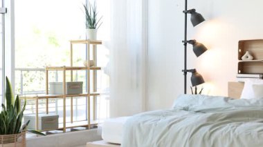 Raflar, lamba, rahat büyük yatak, yan masa ve sandalye yatak odasındaki beyaz duvarın yanında, kamera sağa hareket ediyor.